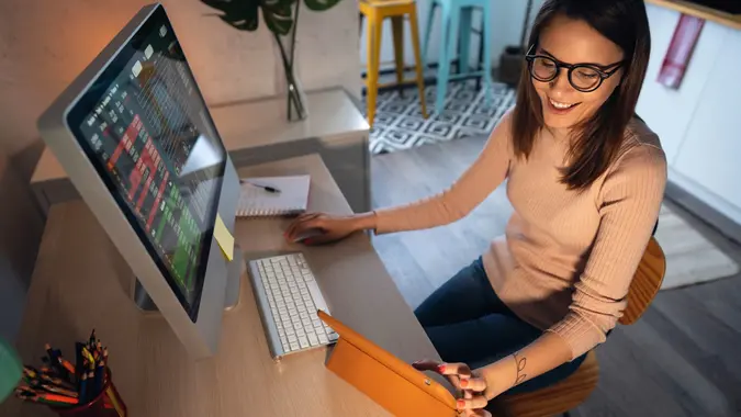 Young woman uses computer and tablet to trade cryptocurrency, stock photo