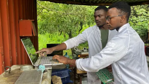 Two men work on computers in a remote location for BBC