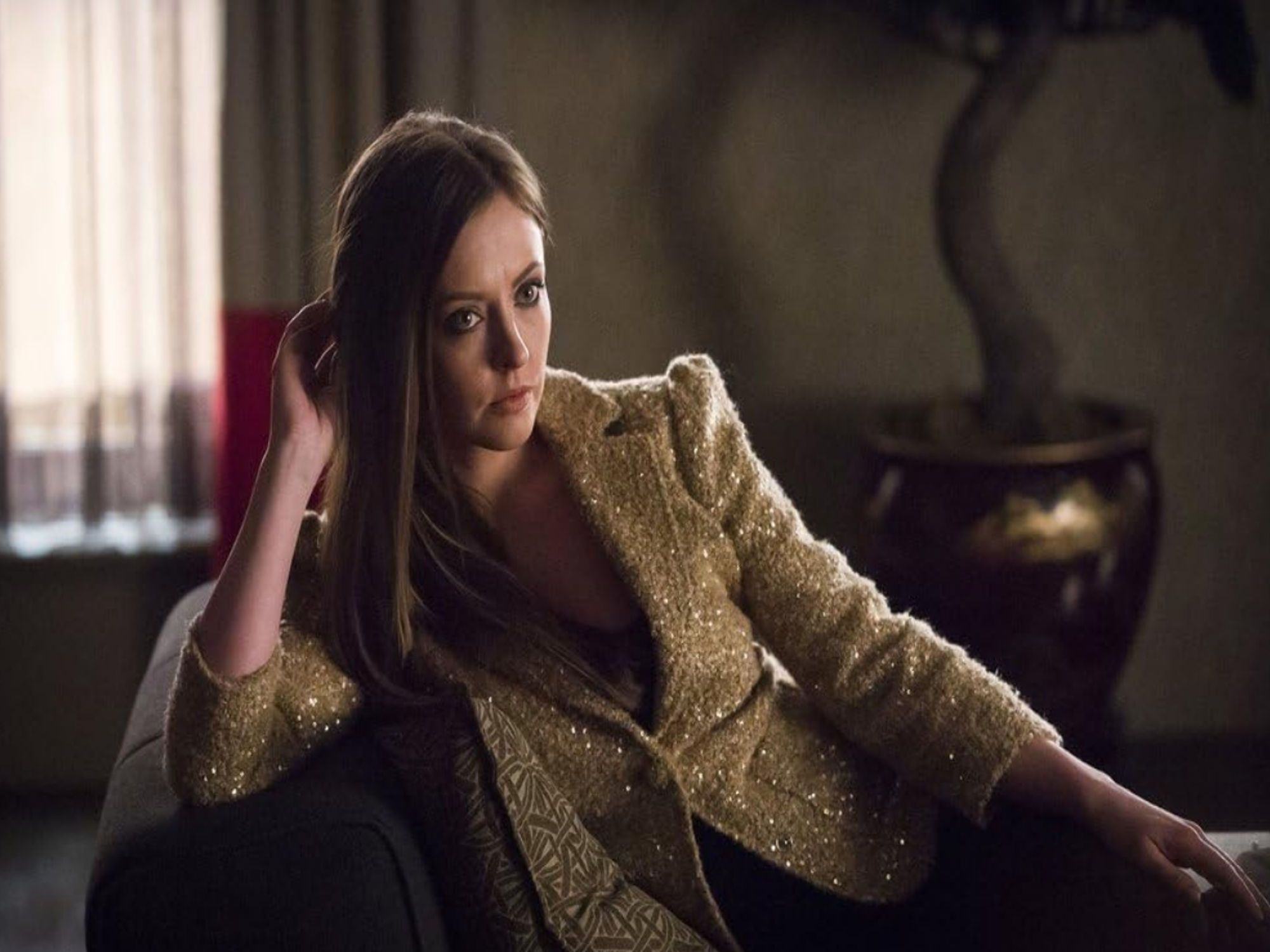 Katherine Isabelle as Margot Verger. She lies on a chaise, with a gold, sparkly jacket on. She looks intensely interested. From NBC Hannibal.