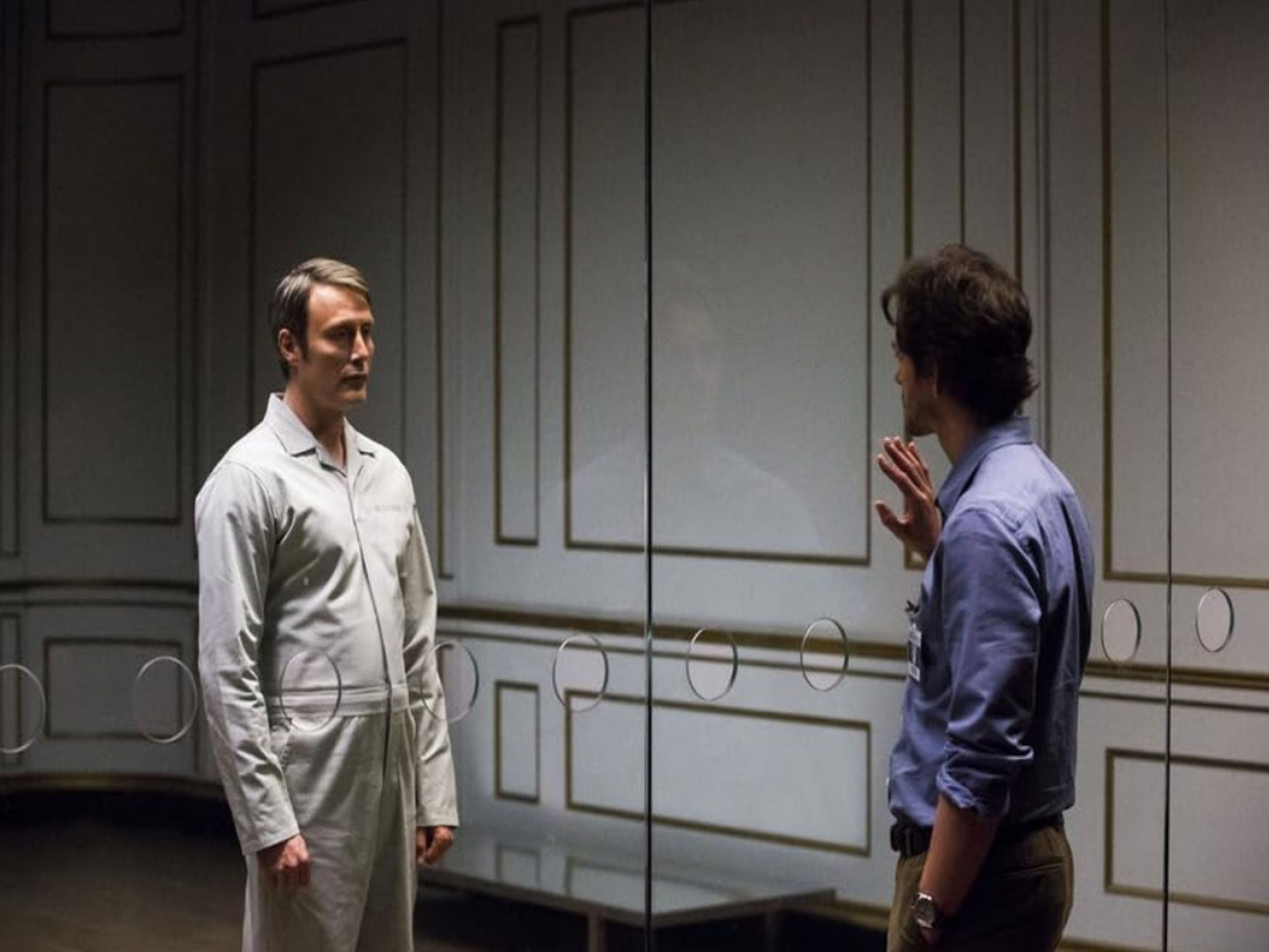 Hugh Dancy as Will Graham and Mads Mikkelsen as Hannibal Lecter stand in front of a glass barrier.  From NBC's Hannibal by Bryan Fuller.