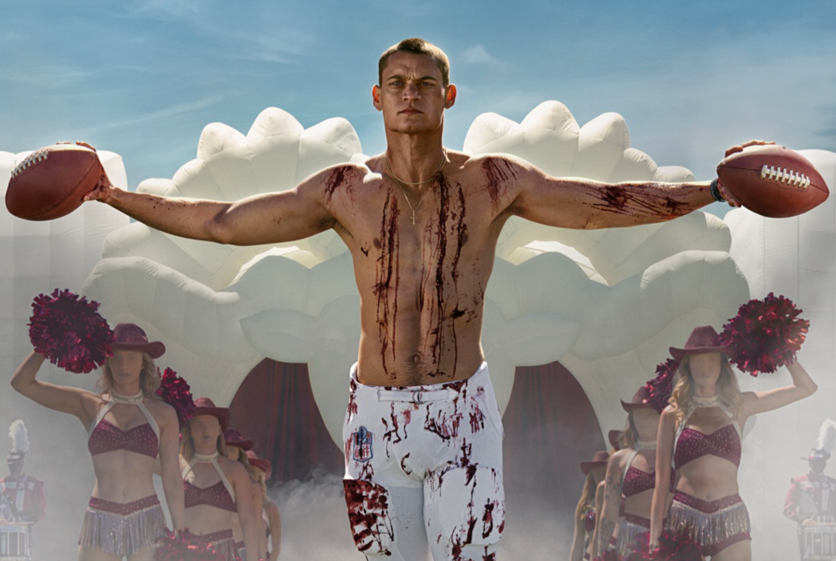 Cam in Him covered in blood and holding two footballs in front of a line of faceless cheerleaders