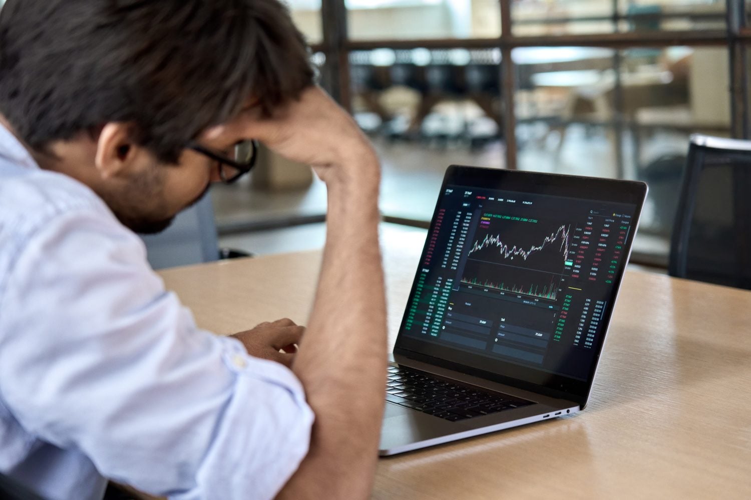 A distressed business person analyzing stock market trends for cryptocurrencies, expressing concern over losses due to market pressures.