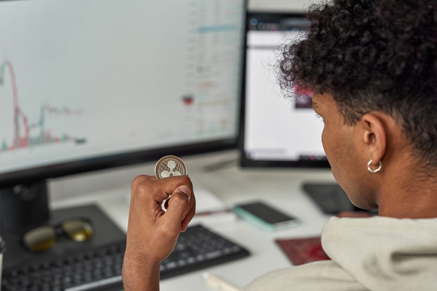 Close up of young male trader holding Ripple XRP crypto currency token, investing in stock market to exchange it while trading from home. Selective focus